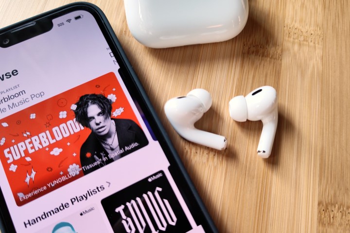 Apple AirPods Pro 2 sitting beside iPhone 14 and charging case.