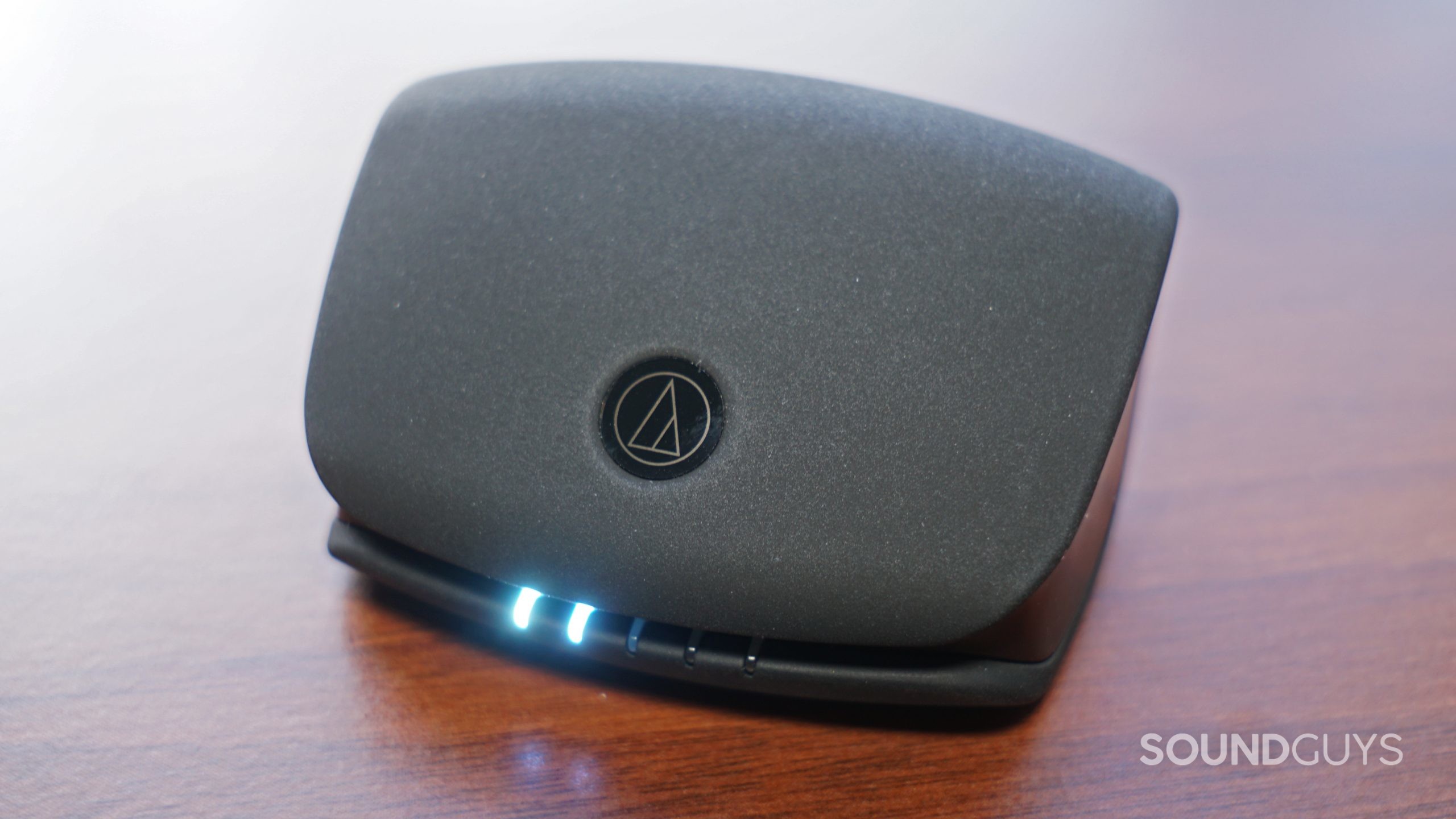 The Audio-Technica ATH-TWX9 charging case sits on a wooden surface.