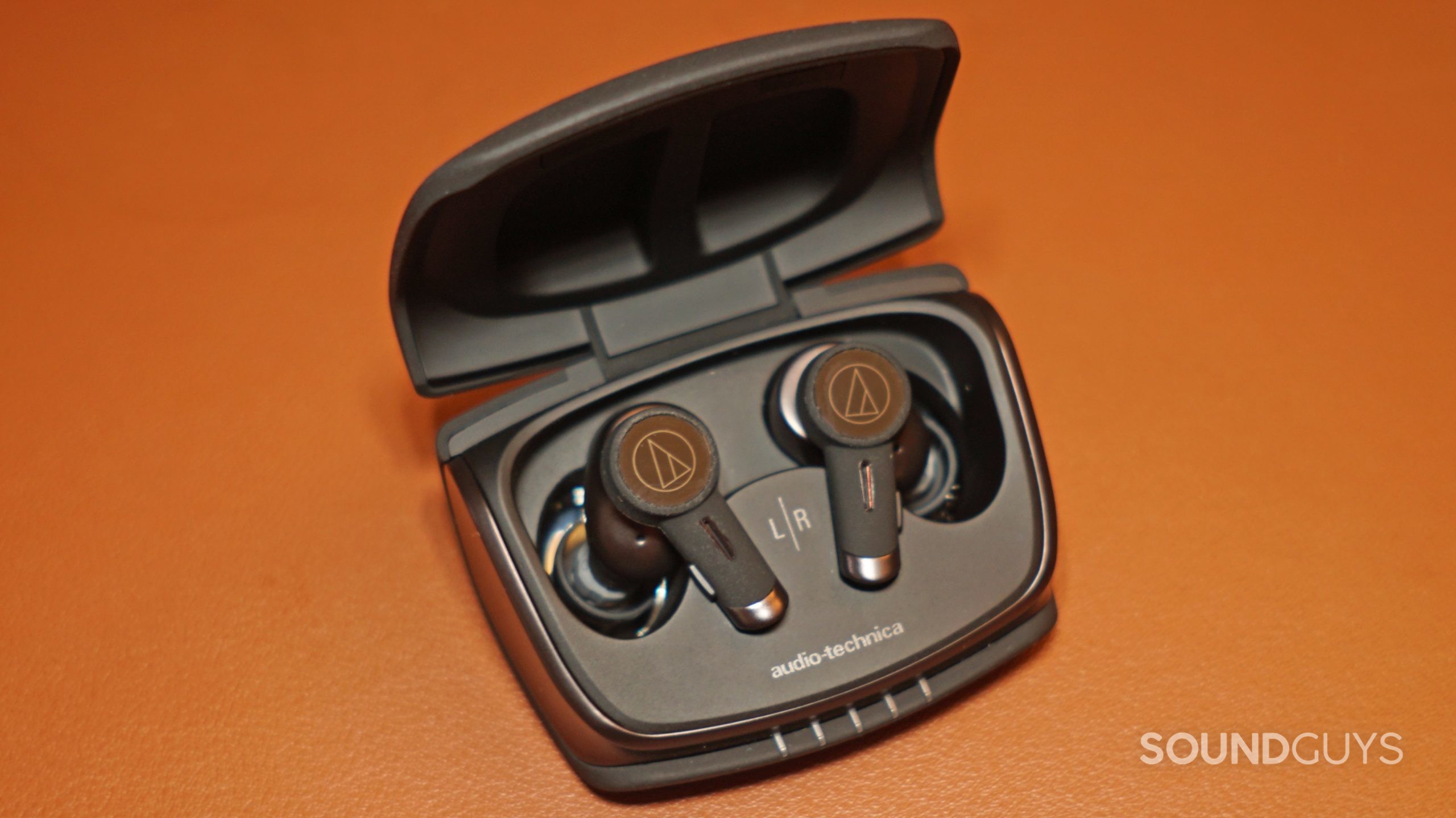 The Audio-Technica ATH-TWX9 earbuds sit in their charing case on a leather surface..