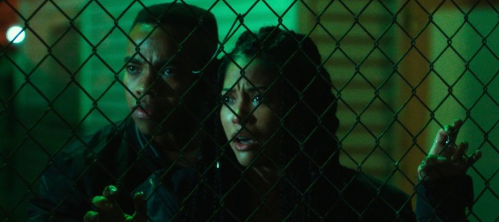 Two people stand up against a fence in the First Purge.