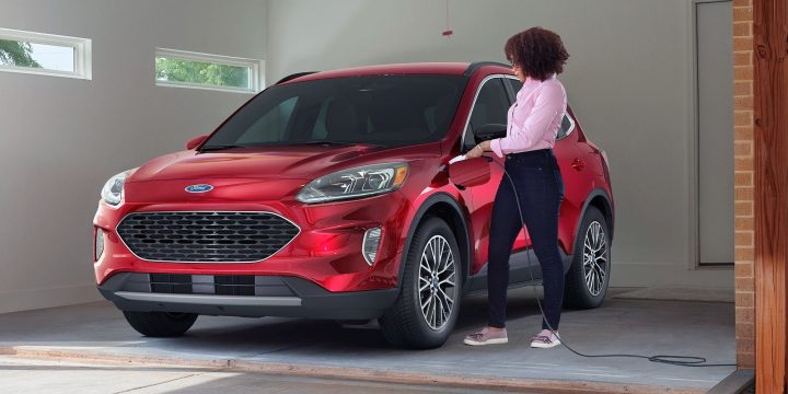 A woman plugs in a red Ford Escape PHEV in a garage. 