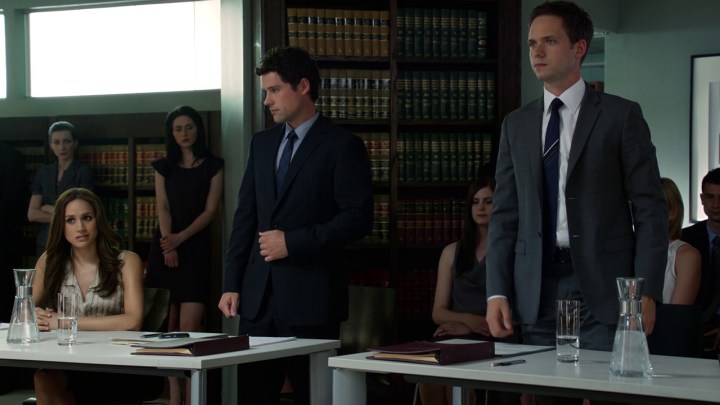 Mike Ross in a mock trial standing up, Rachel sitting on the opposite side with another lawyer in a scene from Suits.
