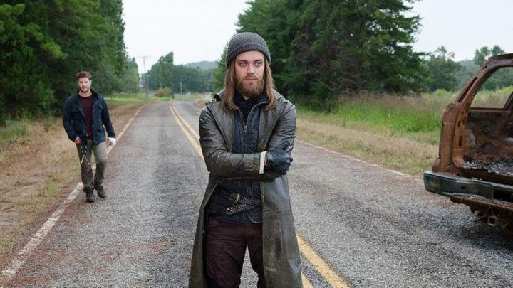 Jesus from The Walking Dead standing in the middle of an empty road, arms folded.