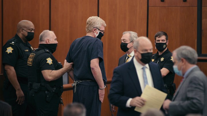 Alex in court wearing a prison jumpsuit and mask with other around him in a scene from Murdaugh Murders on Netflix.