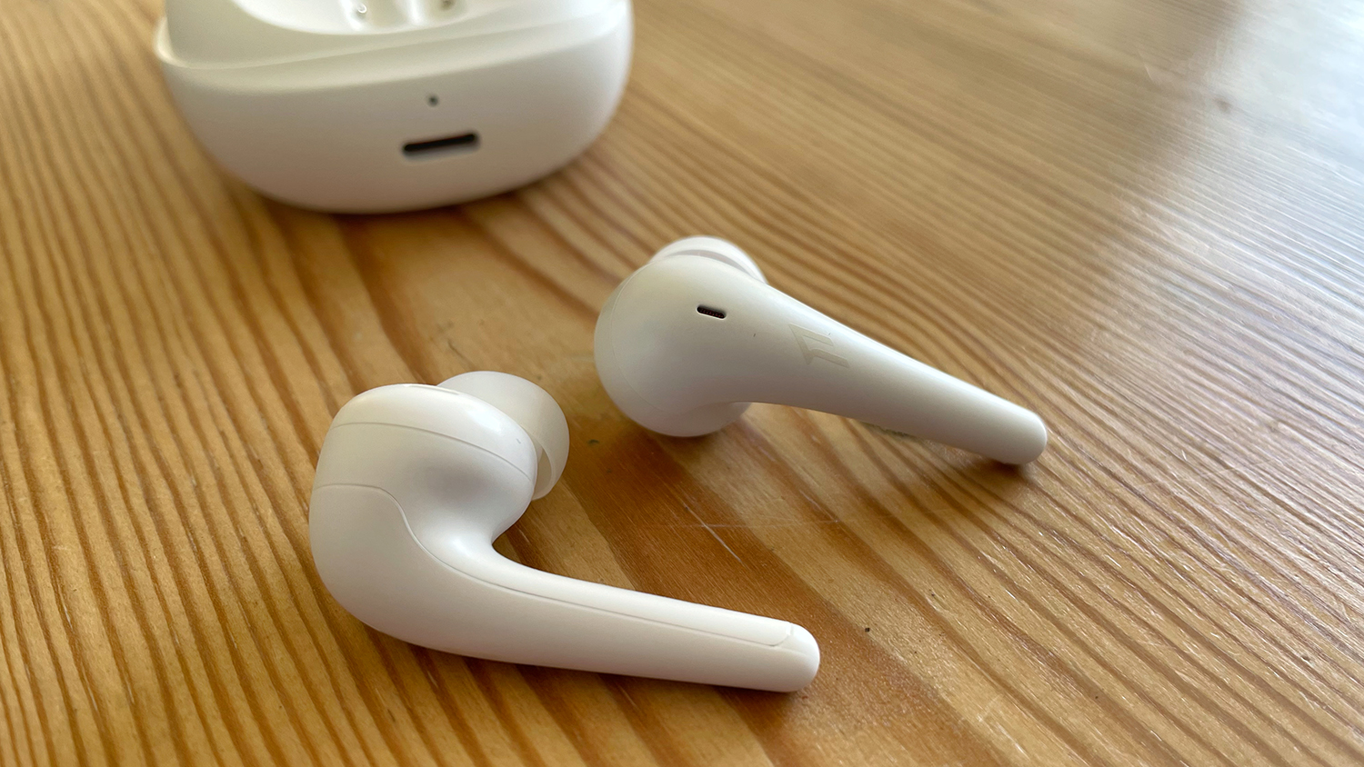 The 1More Aero earbuds pictured on a wooden surface next to their charging case.