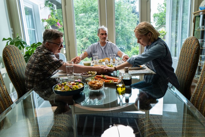 Nathan Lane, Joaquin Phoenix, and Amy Ryan sit around a table together in Beau is Afraid.