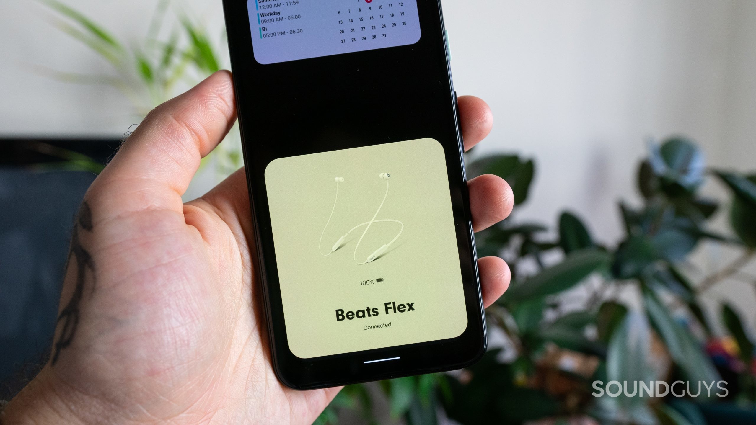 Man holding Android phone in front of plants with Beats Flex pairing card pop-up on the screen.