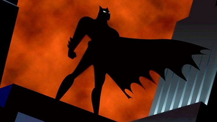 The shadowy silhouette of Batman standing atop a building in Gotham City.