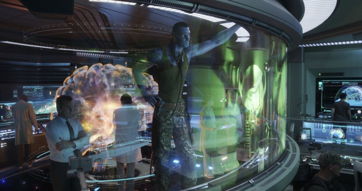 A large Na'vi stands next to a human in a control room in a scene from Avatar: The Way of Water.