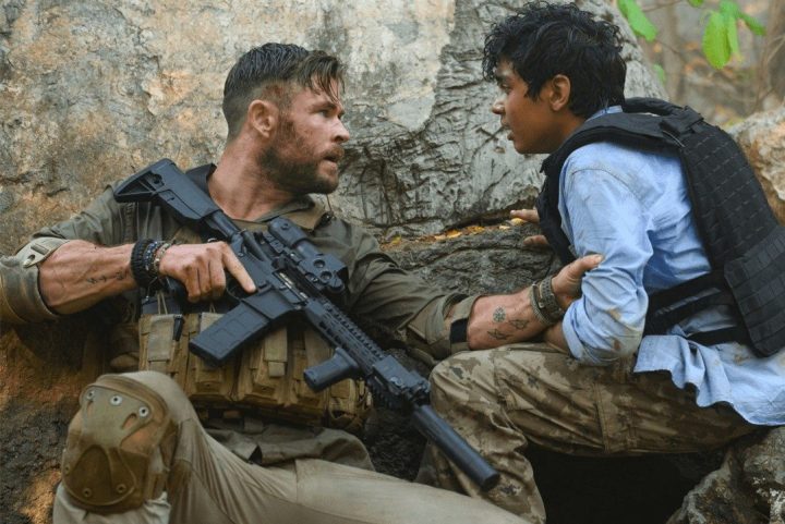 Chris Hemsworth holds a kid and a gun in Extraction.