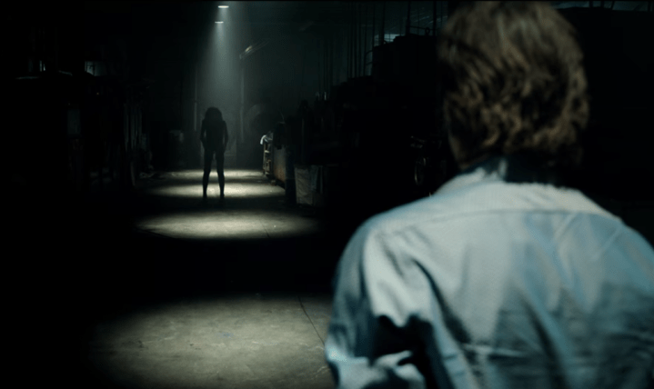 Billy Burke stands in a spotlight in front of an ominous figure in Lights Out.