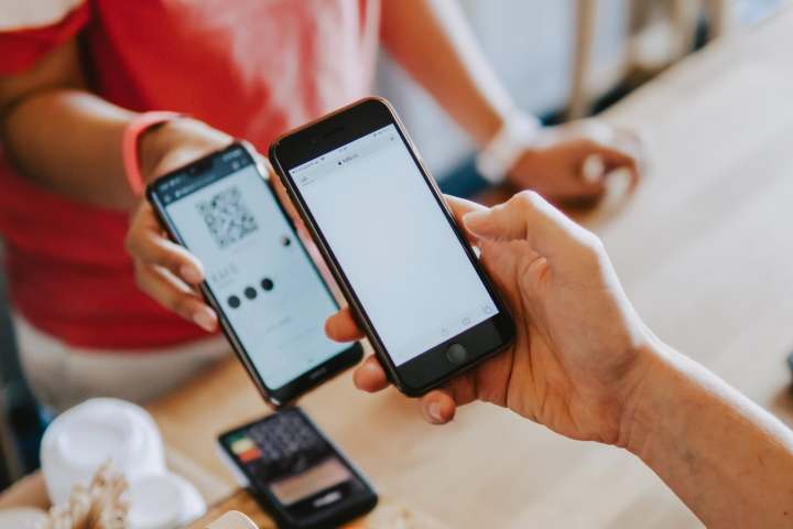 A person holds a smartphone over another smartphone at a retail counter.