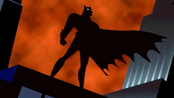 The silhouette of Batman standing atop a building in Gotham.